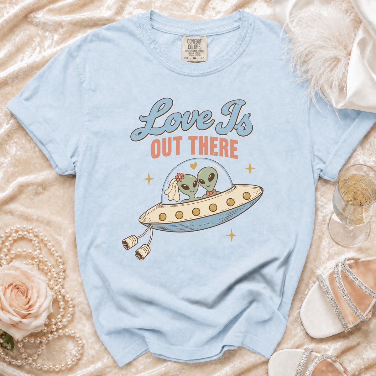 Light blue t-shirt with graphic of two aliens in a UFO, reading "Love Is Out There".