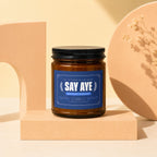Brown candle with "Say Aye" label in navy blue, "Motion Passed," and "Vowed."