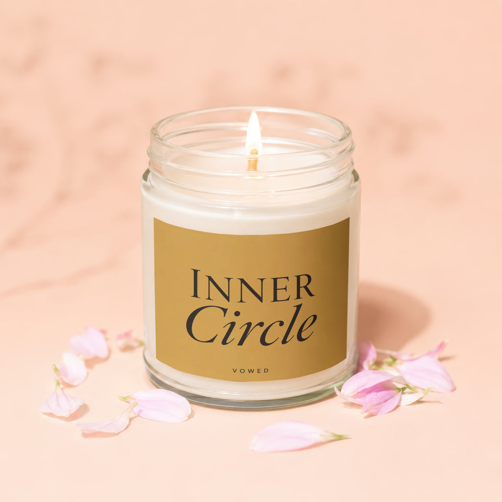 Lit candle in glass jar with "Inner Circle" label and pink petals.