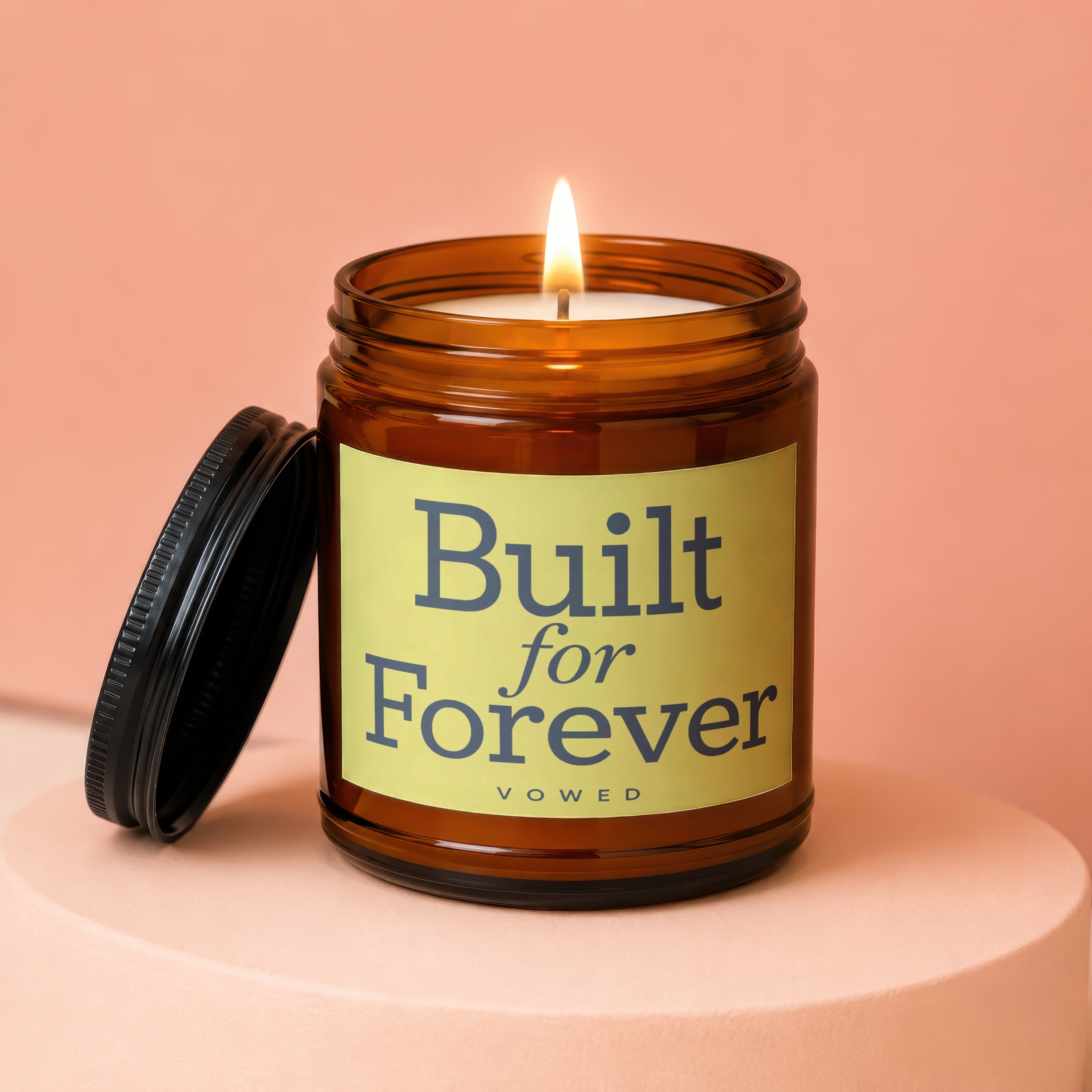 Amber jar candle with lit wick, featuring text "Built for Forever VOWED".