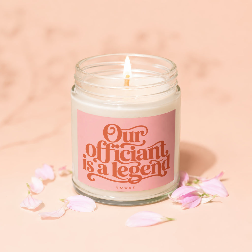 Lit candle with pink label reading "Our Officiant is a Legend" and "VOWED".