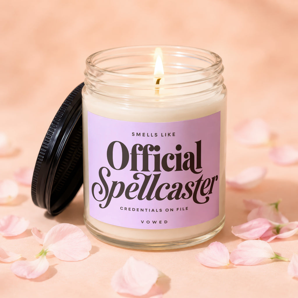 Lit candle in glass jar with "Official Spellcaster" text on lavender label.