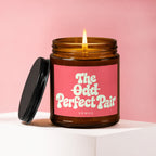 Brown glass candle with lit wick, pink label reads "The Odd Perfect Pair".