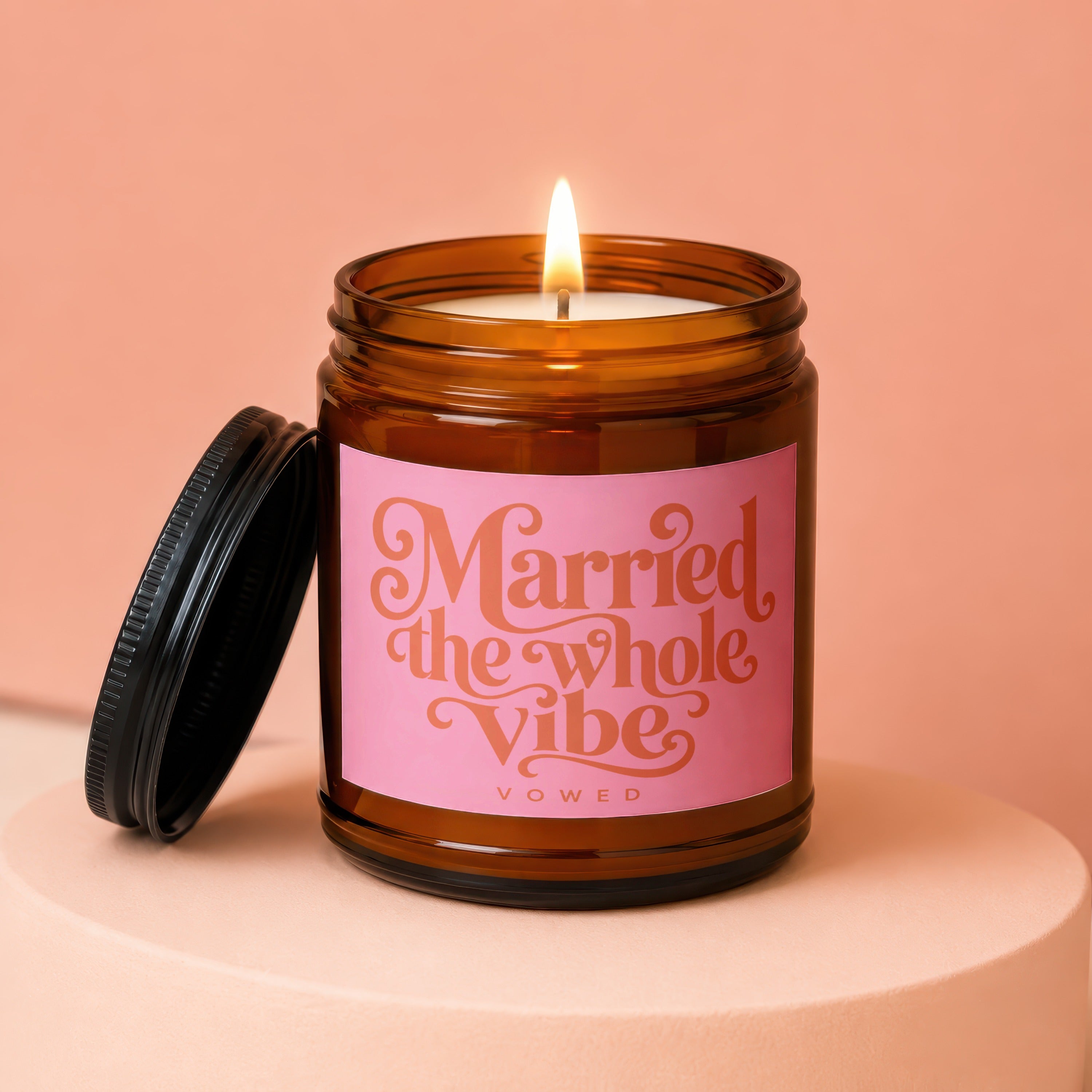 Lit candle in amber jar with pink label saying "Married the whole vibe VOWED".