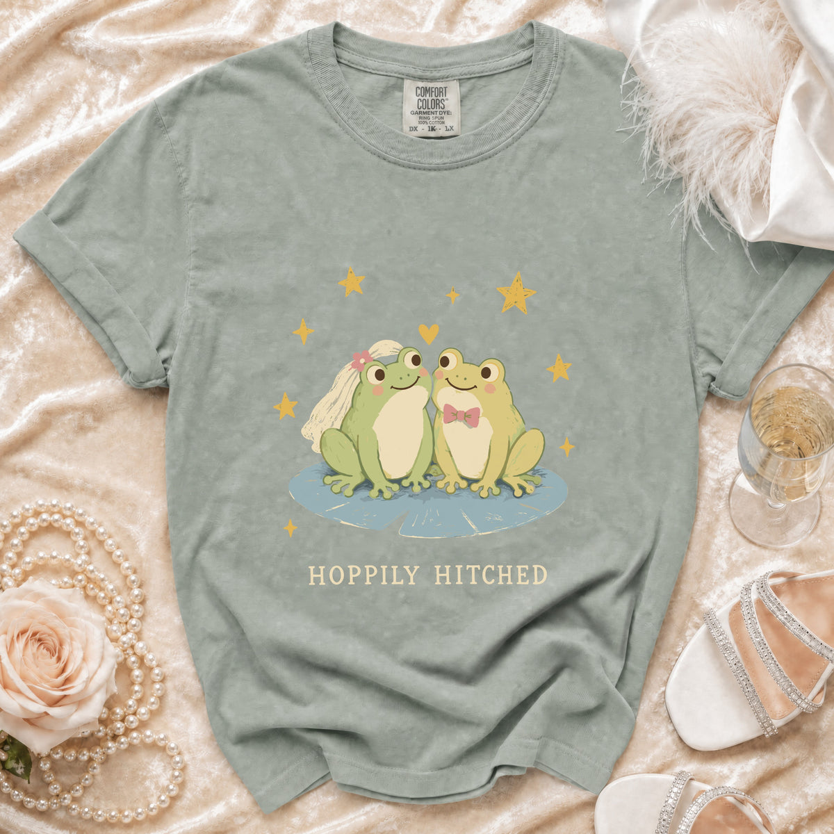 T-shirt with two cartoon frogs, wedding veil, bow tie, and "Happily Hitched" text.