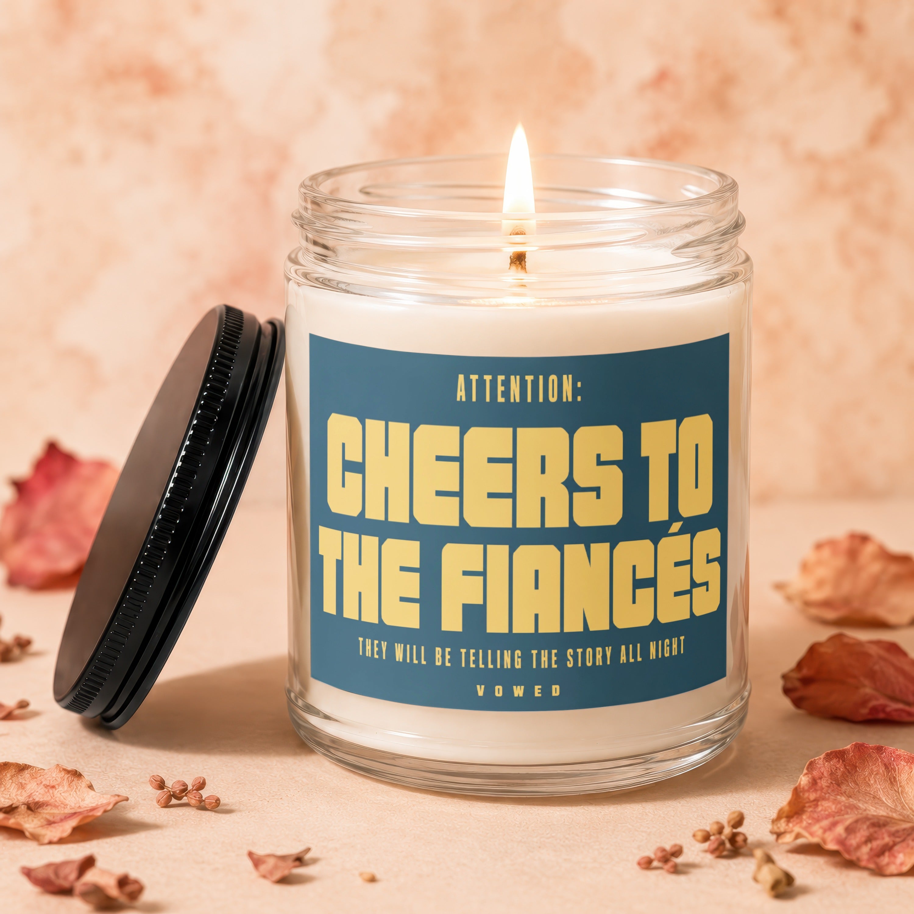 Candle reading "Cheers to the Fiancés" with lid and dried botanicals.