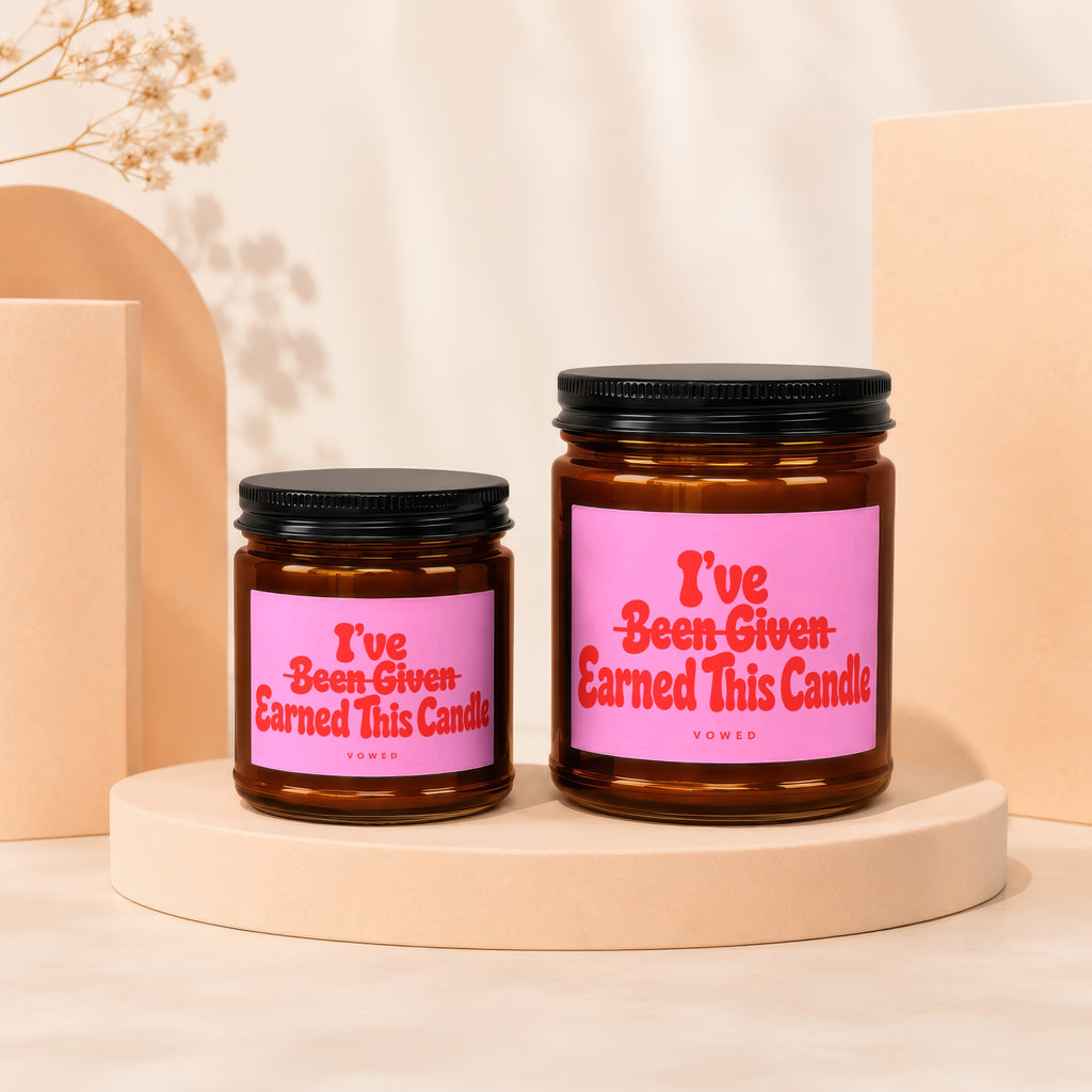 Two amber glass candles with pink labels that read "I've Been Given Earned This Candle."