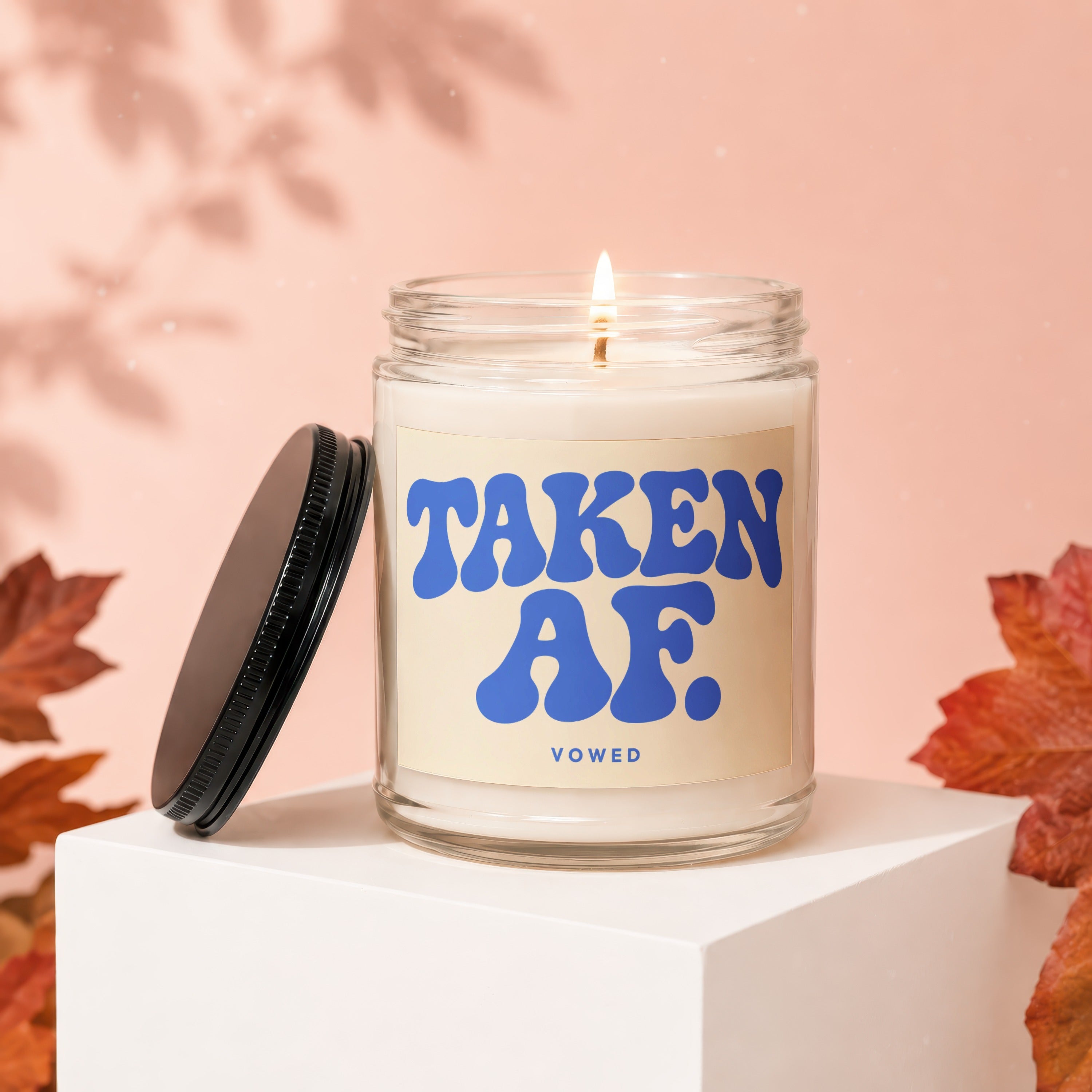 Scented candle with "TAKEN AF. VOWED" text on a pale background.