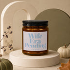 Amber candle with "Wife Era Pending" text on label, on a pedestal.