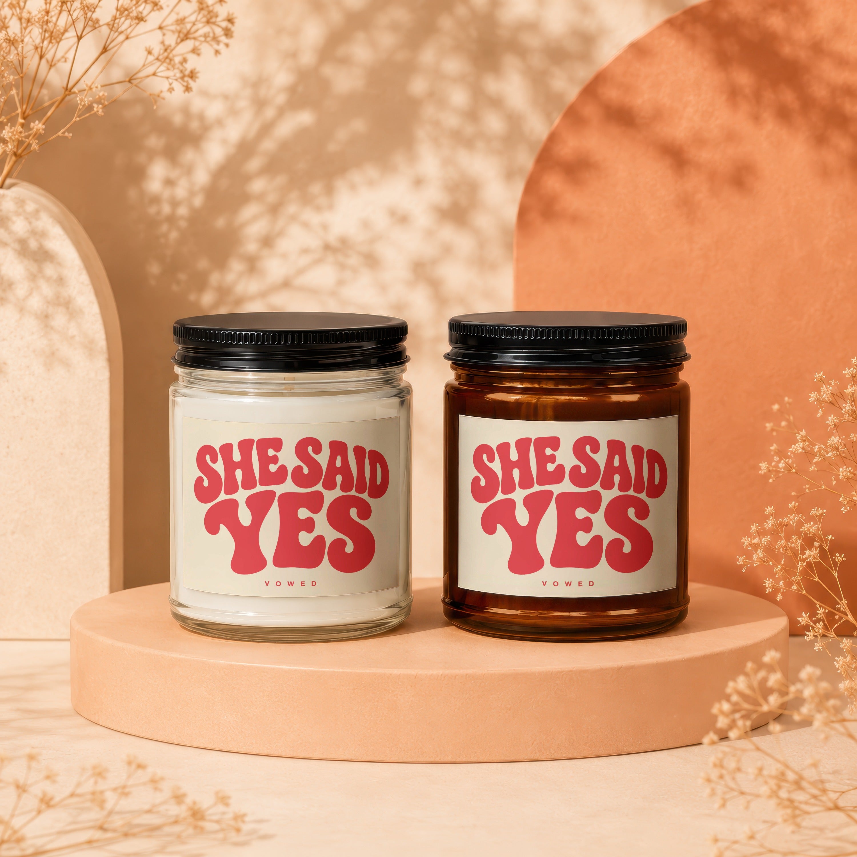 Two candles with "SHE SAID YES" text on cream labels, one in a clear jar, one in amber.