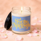 Candle labeled "For the Newlyweds VOWED" with lit wick, surrounded by pink petals.