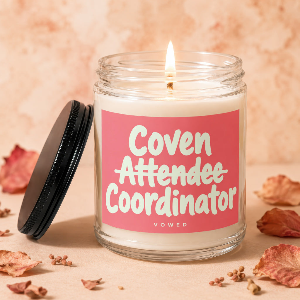 Candle with lit wick, the label reads "Coven Attendee Coordinator VOWED."