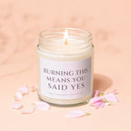 Candle with text "BURNING THIS MEANS YOU SAID YES" and pink petals.
