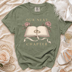 Green t-shirt with an open book, rings, roses, and text "Our Next Chapter".