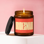 Amber glass candle with lit wick and black lid, labeled "BRIDESMAID VOCWED".