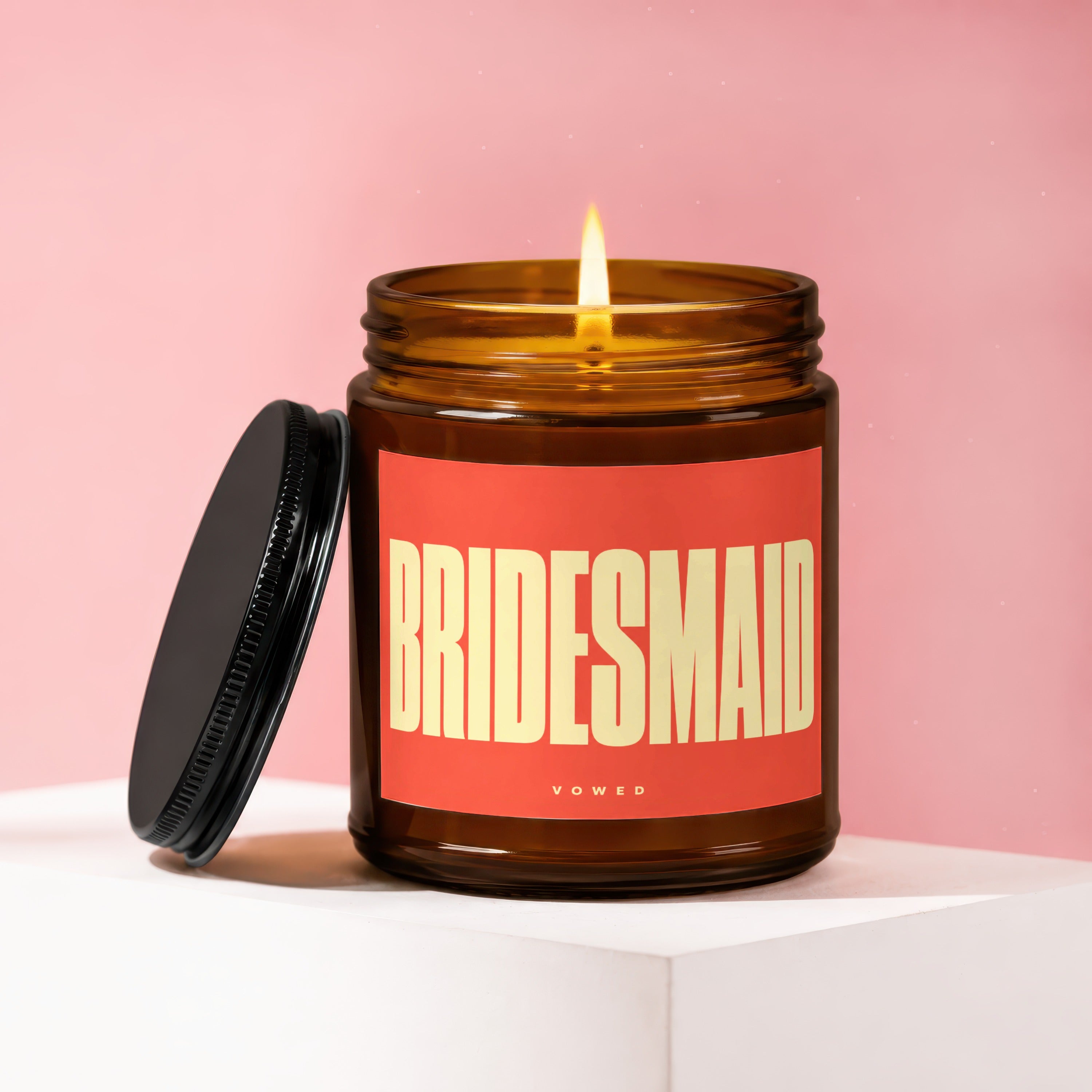 Amber glass candle with lit wick and black lid, labeled "BRIDESMAID VOCWED".