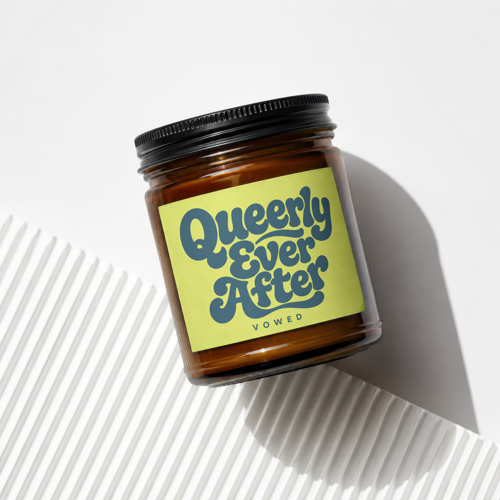 Amber jar candle with yellow label reading "Queerly Ever After Vowed."