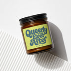 Amber jar candle with yellow label reading "Queerly Ever After Vowed."