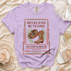 T-shirt with "Reckless in Texas" and "Olivia's Bach" text and cowboy boot graphic.