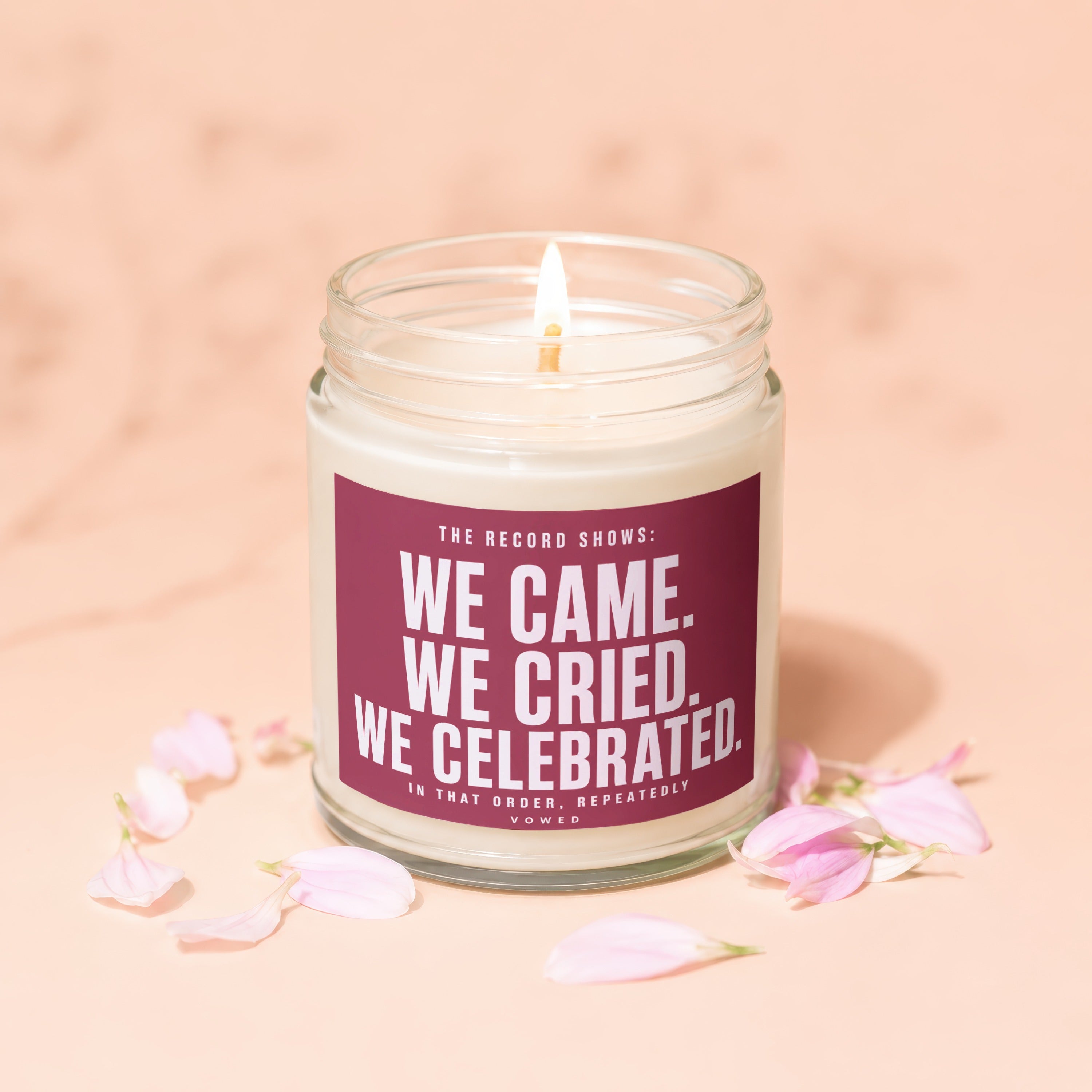 Candle with text "We Came. We Cried. We Celebrated. In That Order, Repeatedly" surrounded by petals.