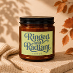 Amber jar candle with "Ringed and Radiant VOWED" label on textured stone.