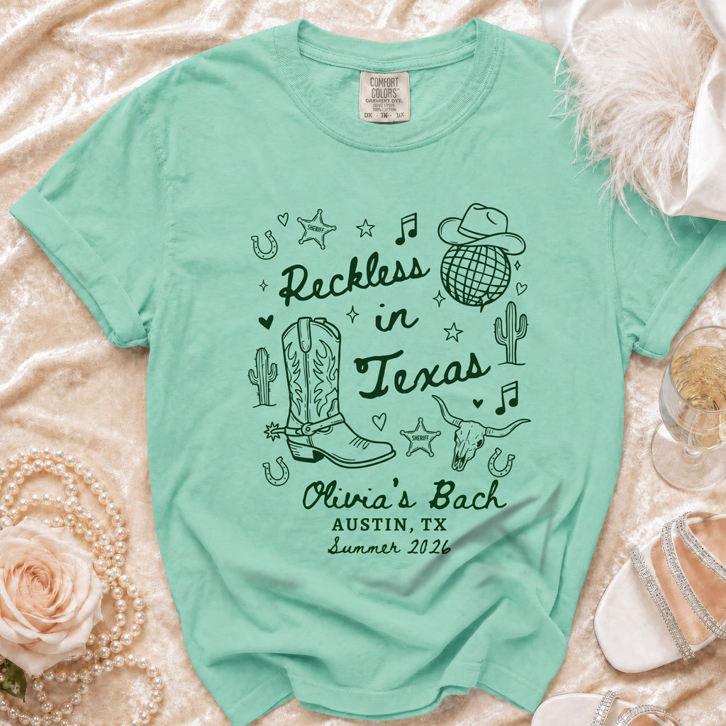 Teal t-shirt with "Reckless in Texas" and cowboy boot design.