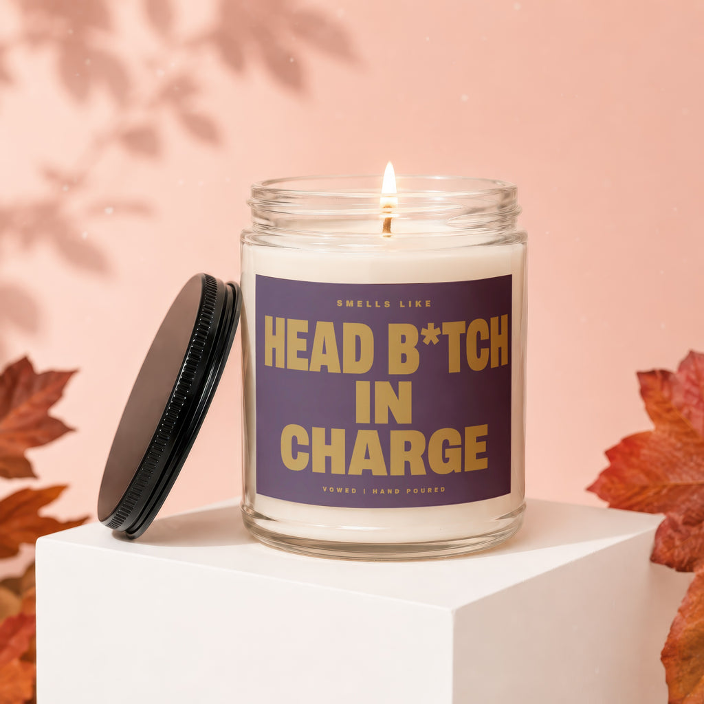 Scented candle with gold text "Smells like HEAD B*TCH IN CHARGE" on purple label.