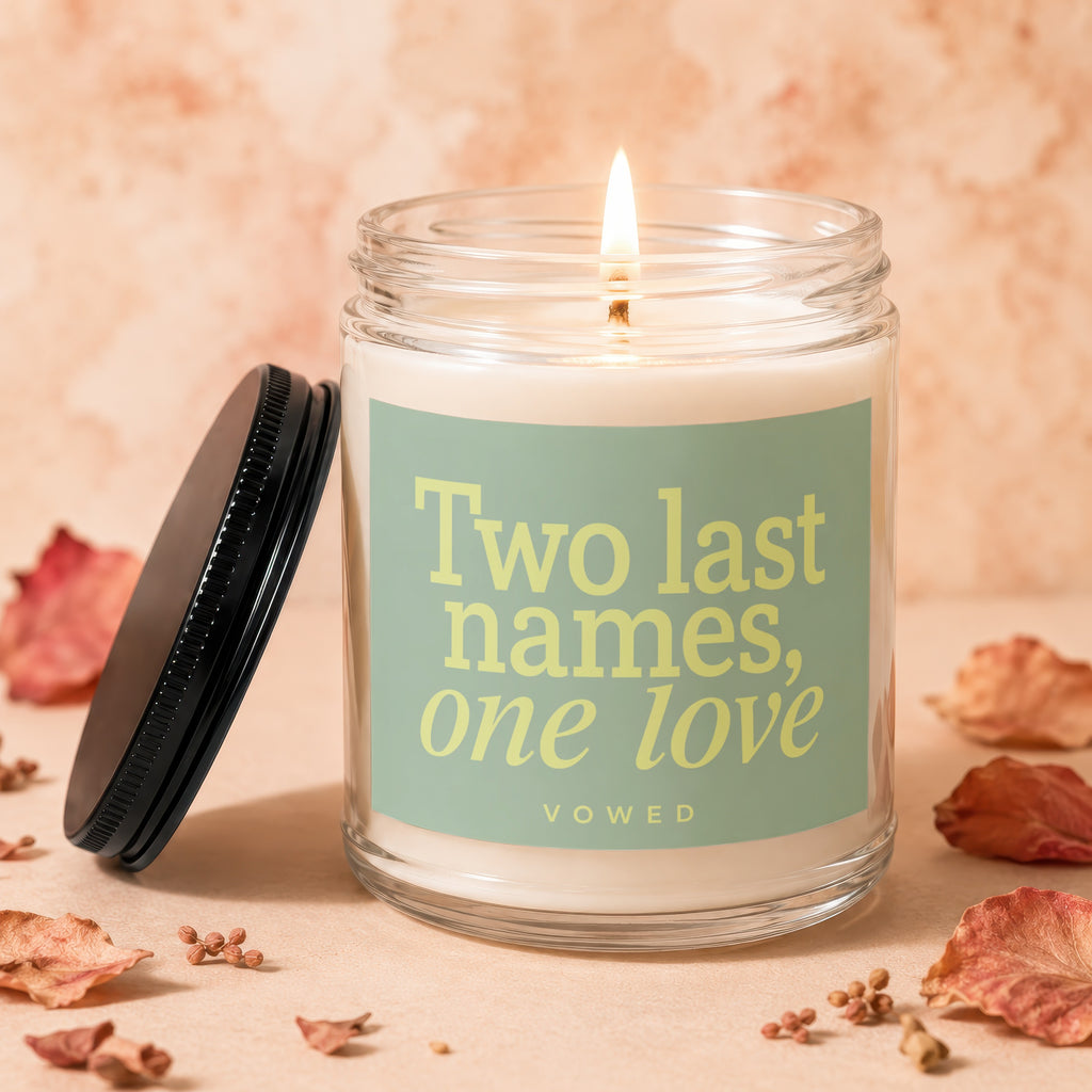 Glass candle with lit wick and label reading "Two last names, one love vōwed".
