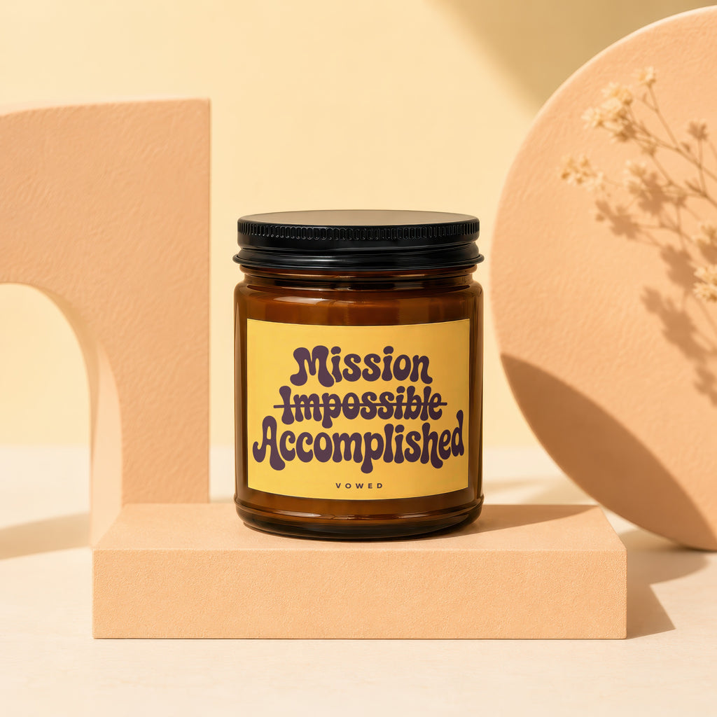 Amber glass candle with "Mission Impossible Accomplished" printed on yellow label.