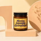 Amber glass candle with "Mission Impossible Accomplished" printed on yellow label.