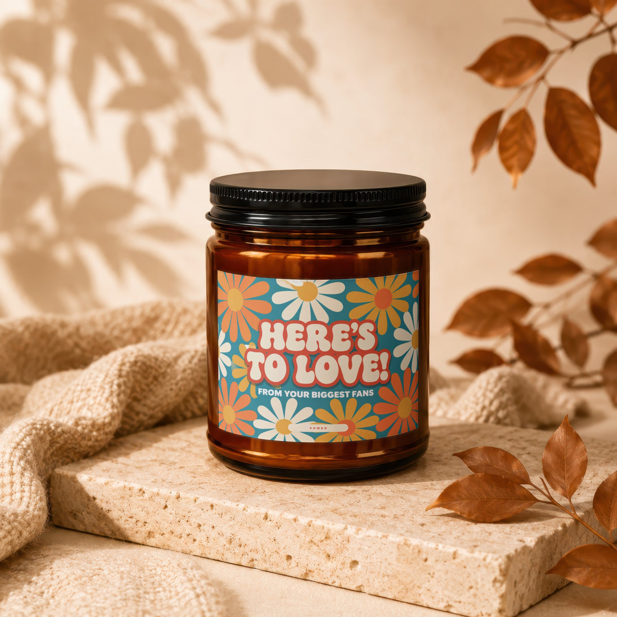 Amber candle with retro flower label reading "HERE'S TO LOVE! FROM YOUR BIGGEST FANS."