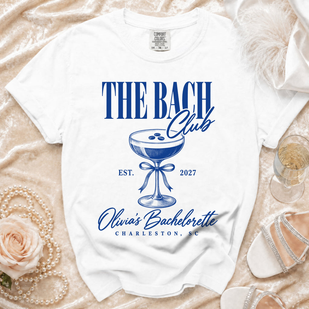 White t-shirt with "The Bach Club" text, cocktail glass, and "Olivia's Bachelorette Charleston, SC" in blue.