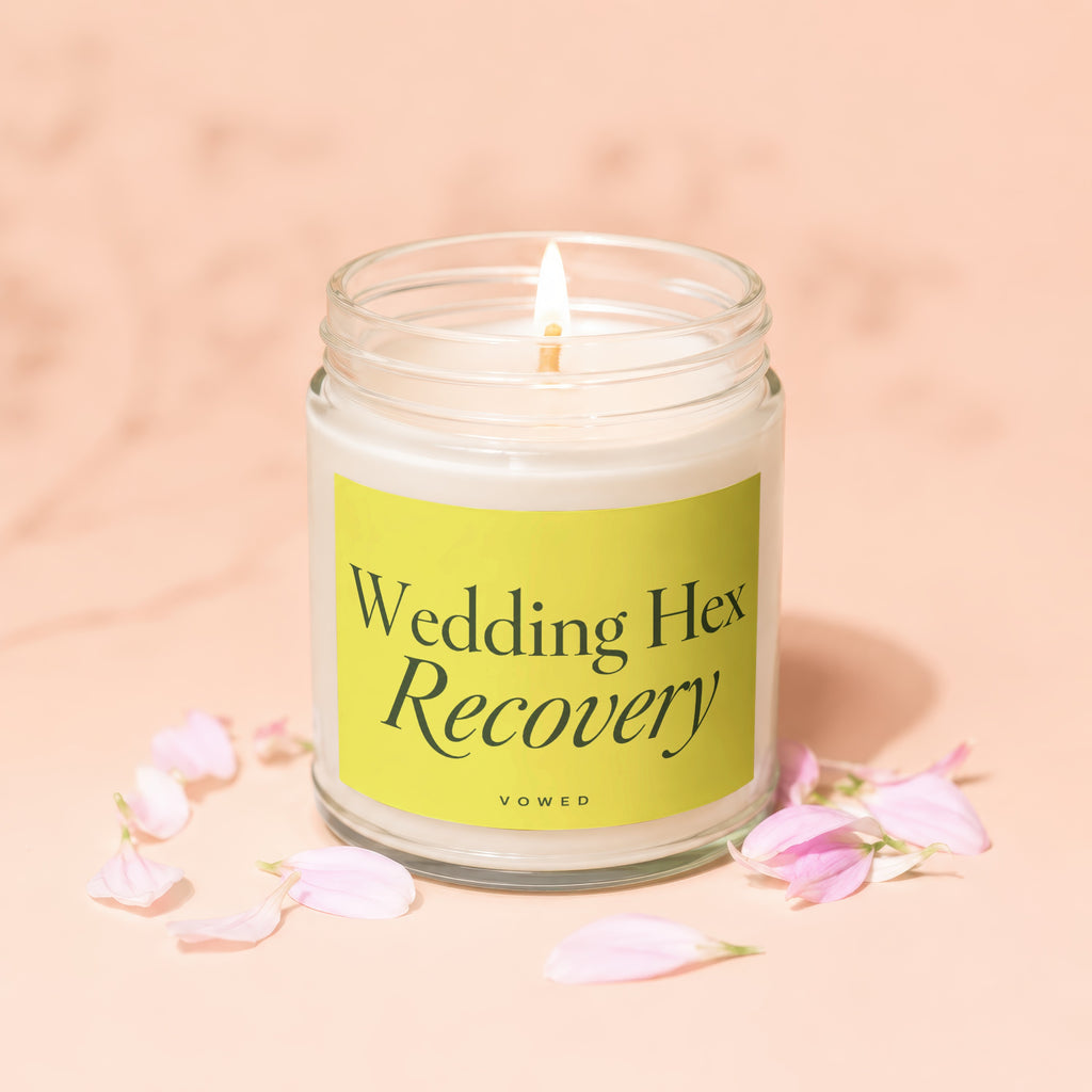 Candle with "Wedding Hex Recovery" and "vowed" text on a yellow label surrounded by petals.