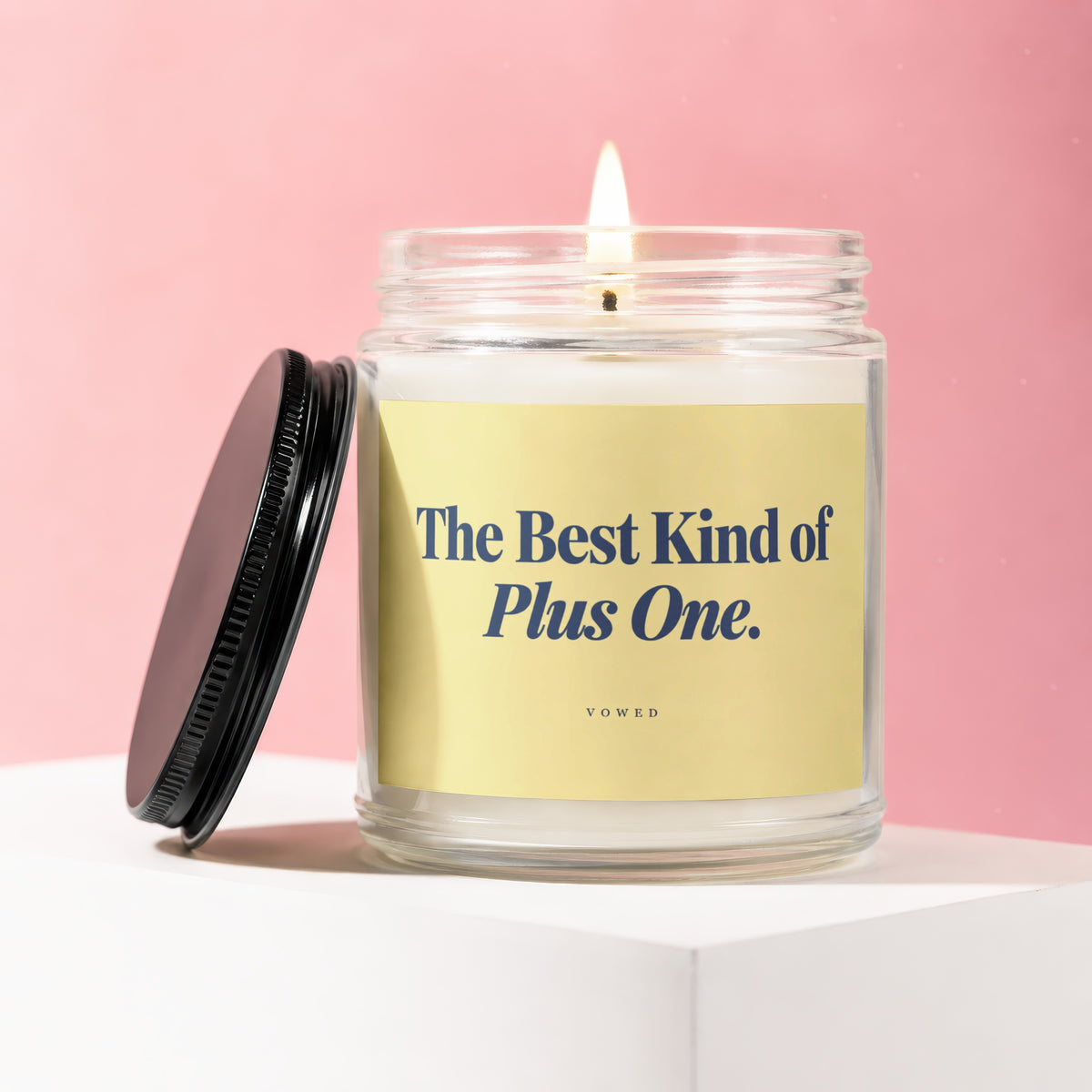 Lit candle in a glass jar with a yellow label that reads "The Best Kind of Plus One."