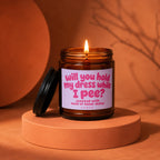 Amber jar candle with lit wick and "will you hold my dress while I pee?" text.