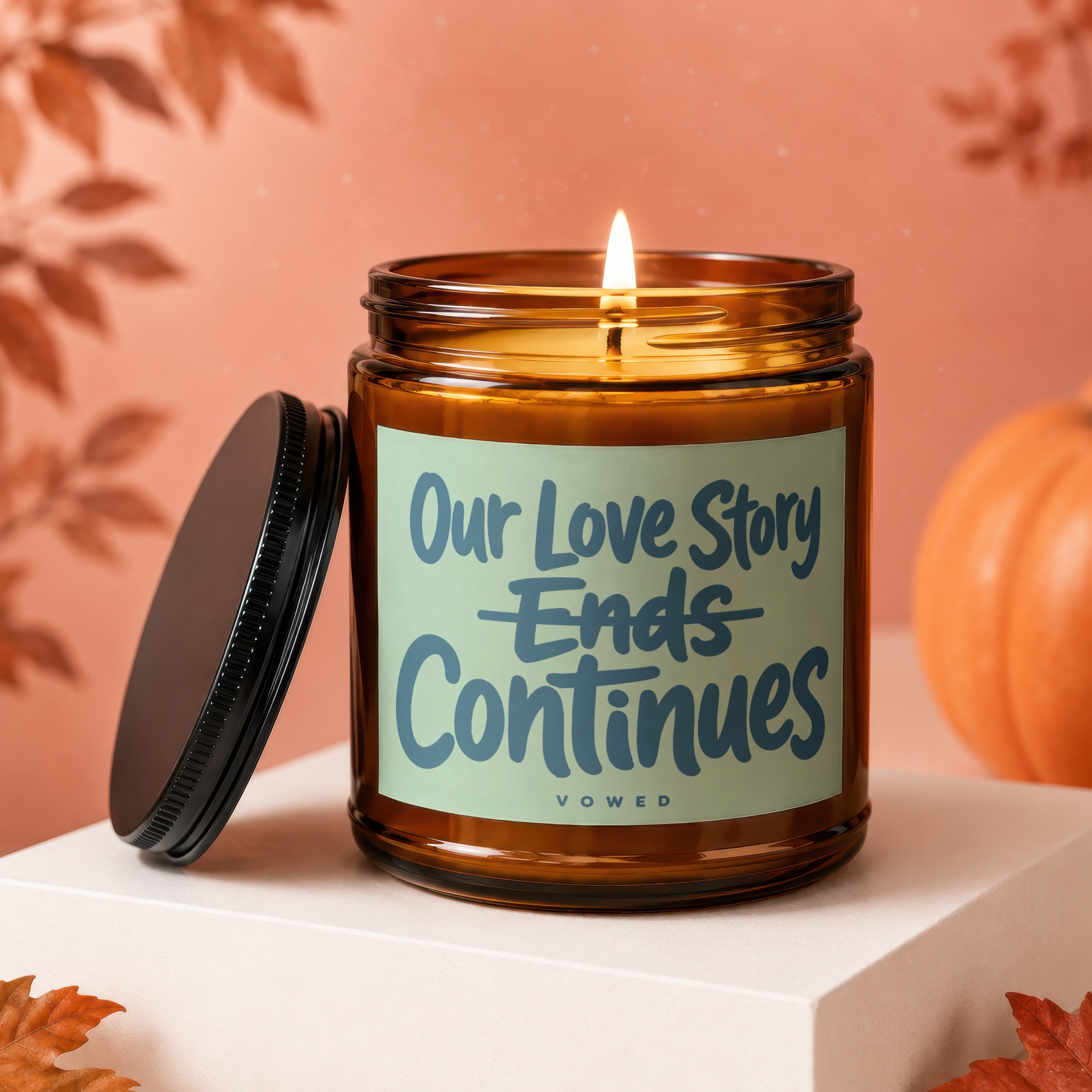 Amber candle with lit flame and lid off; reads "Our Love Story Ends Continues".