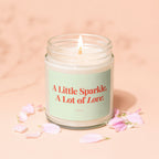 Lit candle in glass jar with "A Little Sparkle, A Lot of Love" text.