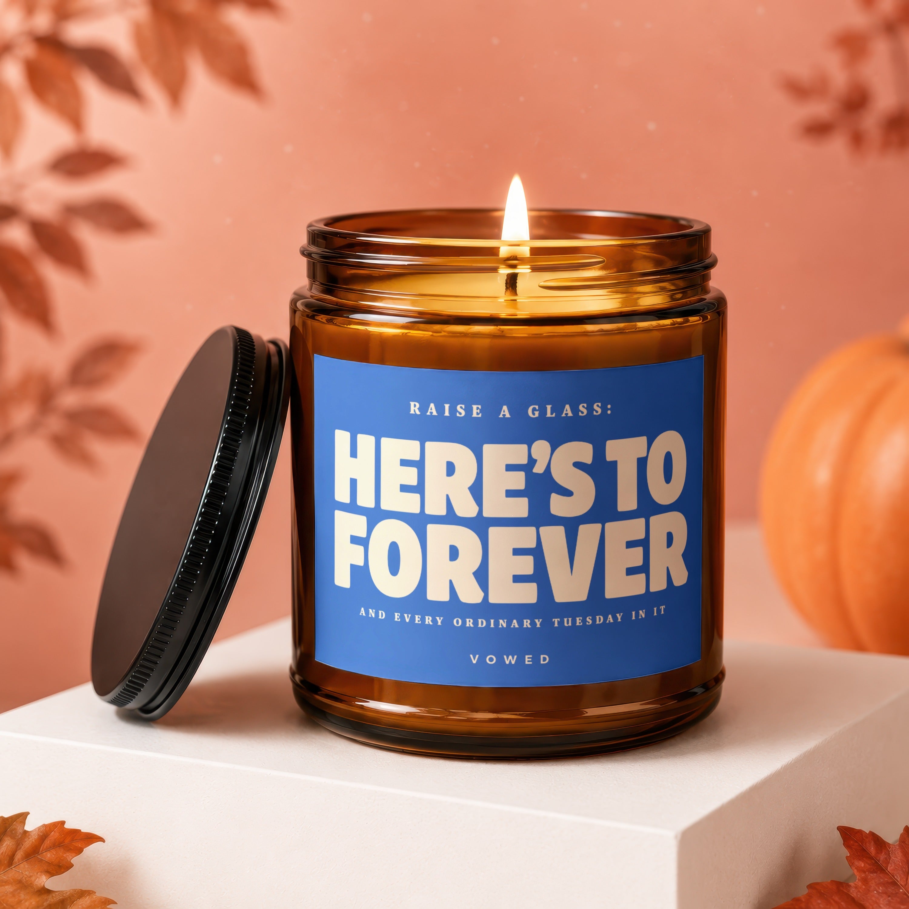 Amber glass candle with blue label reading "Here's to Forever; Vowed".