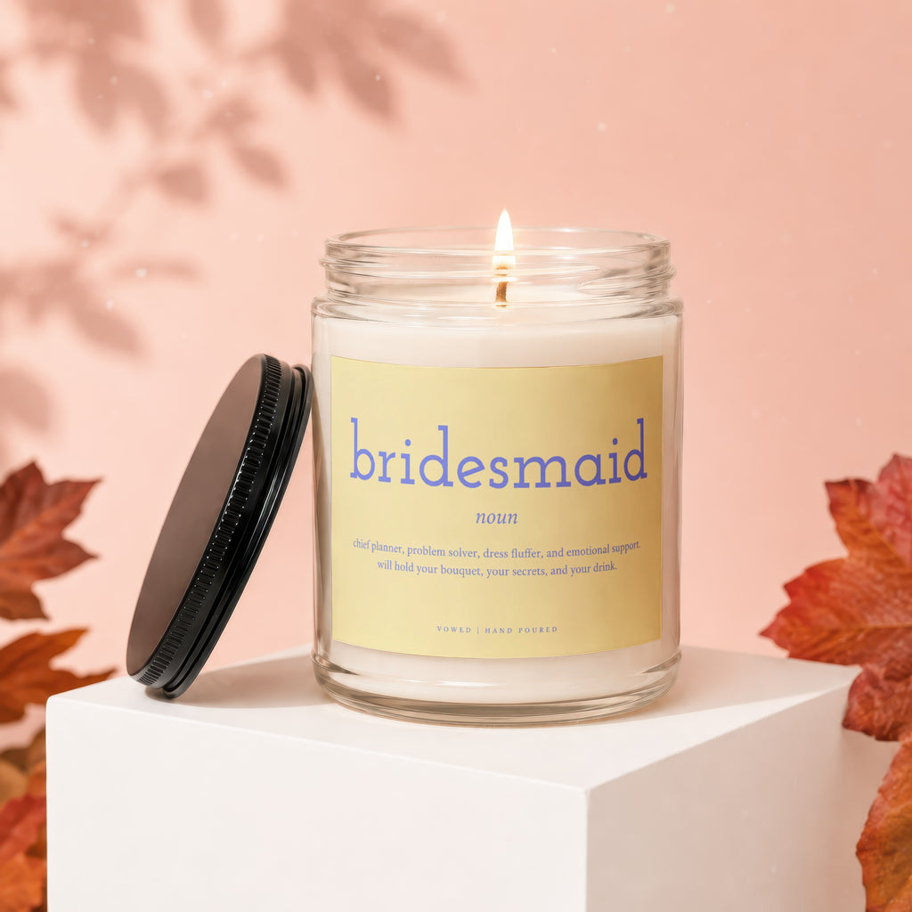 Glass candle with "bridesmaid" definition label, lit wick, and black lid.