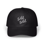 A black baseball cap features the white embroidered cursive text Wild Wild on the front.