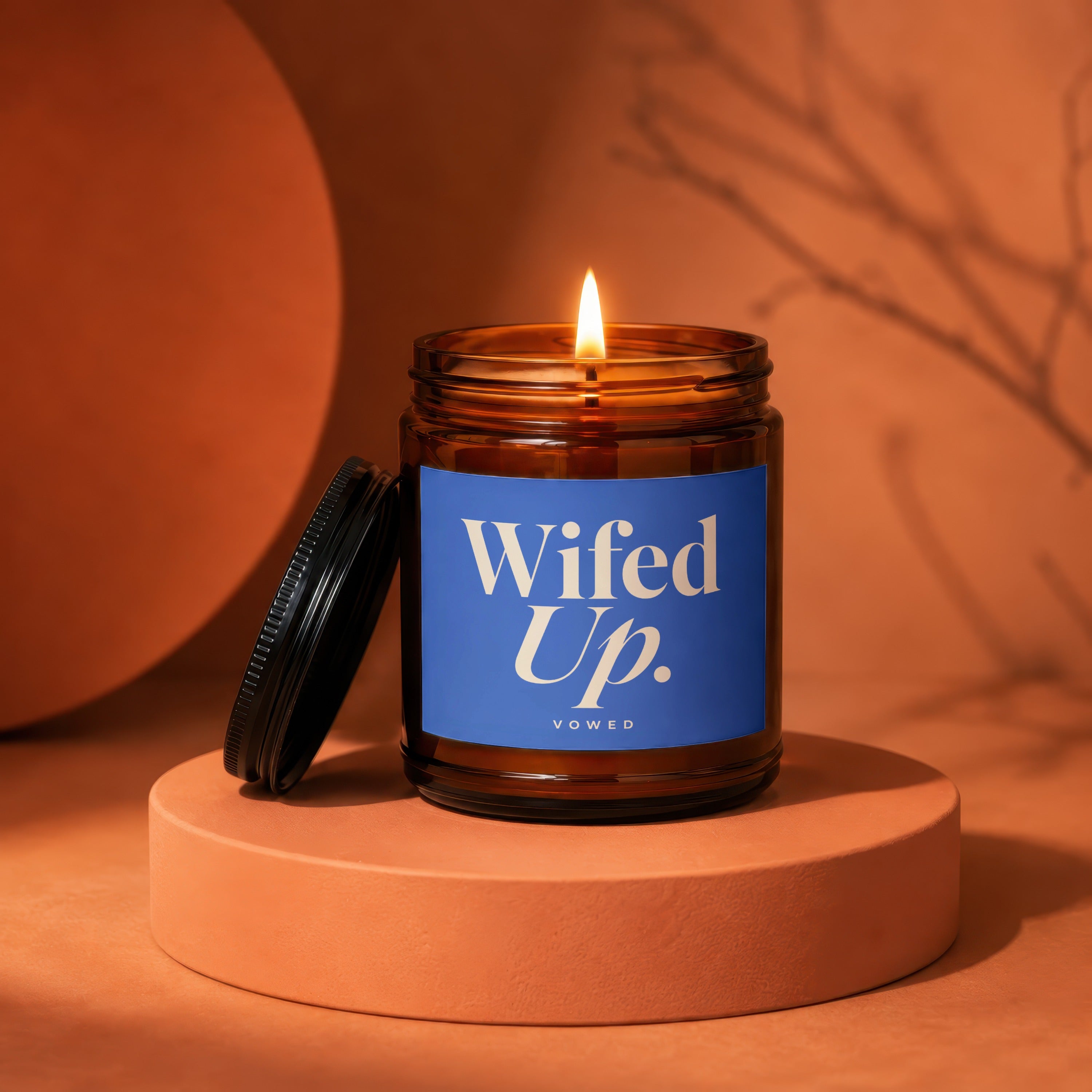 Amber jar candle with lit flame, blue label reads "Wifed Up. VOWED".