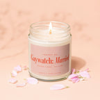 Candle with "Gaywatch: Married" label, lit flame, and pink petals.