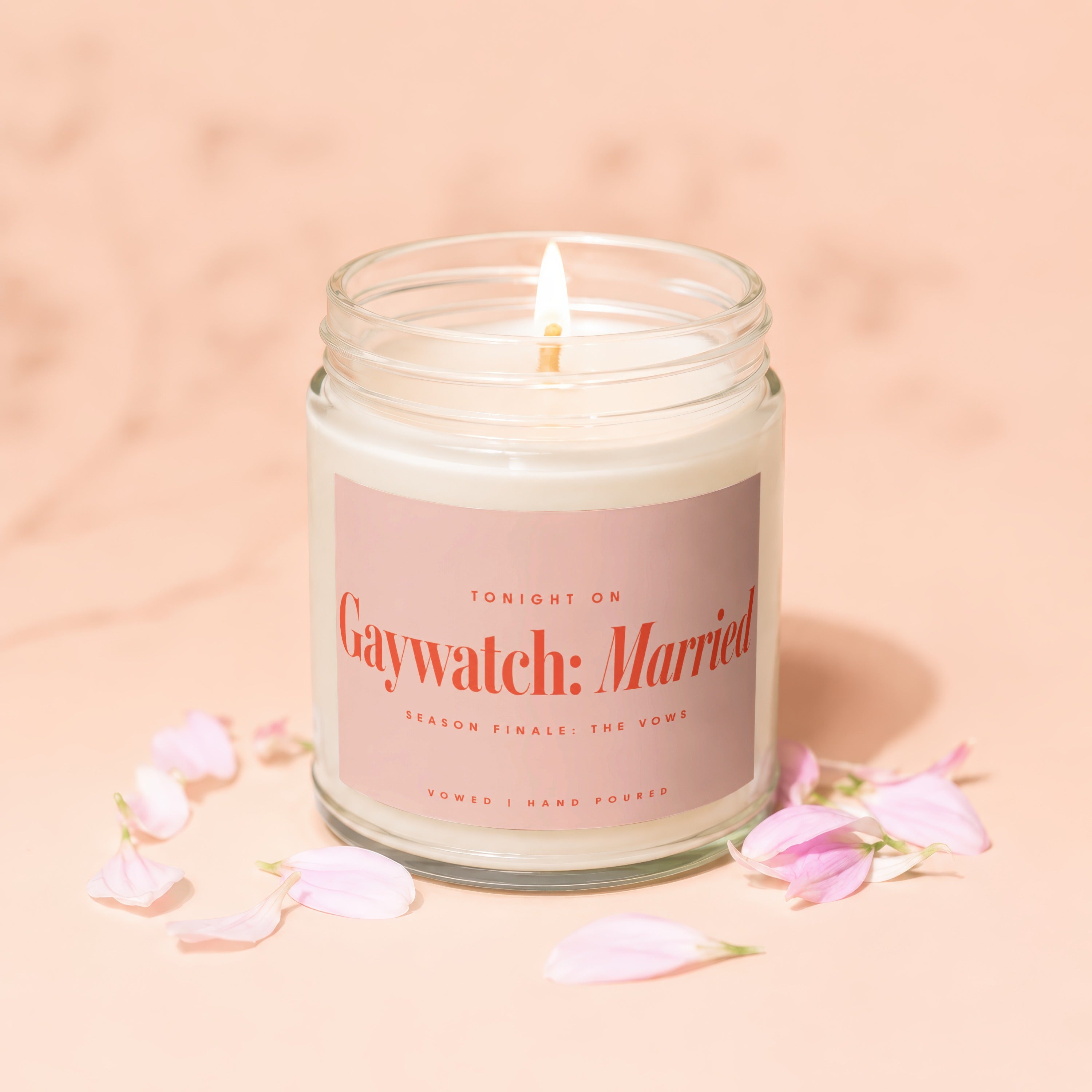 Candle with "Gaywatch: Married" label, lit flame, and pink petals.