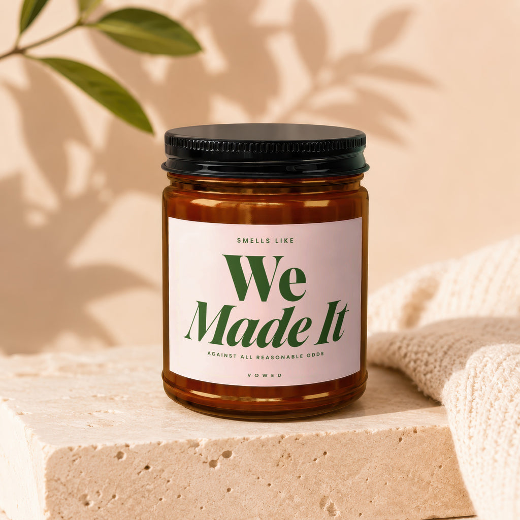 Candle with black lid, amber glass jar, and label reading "We Made It"