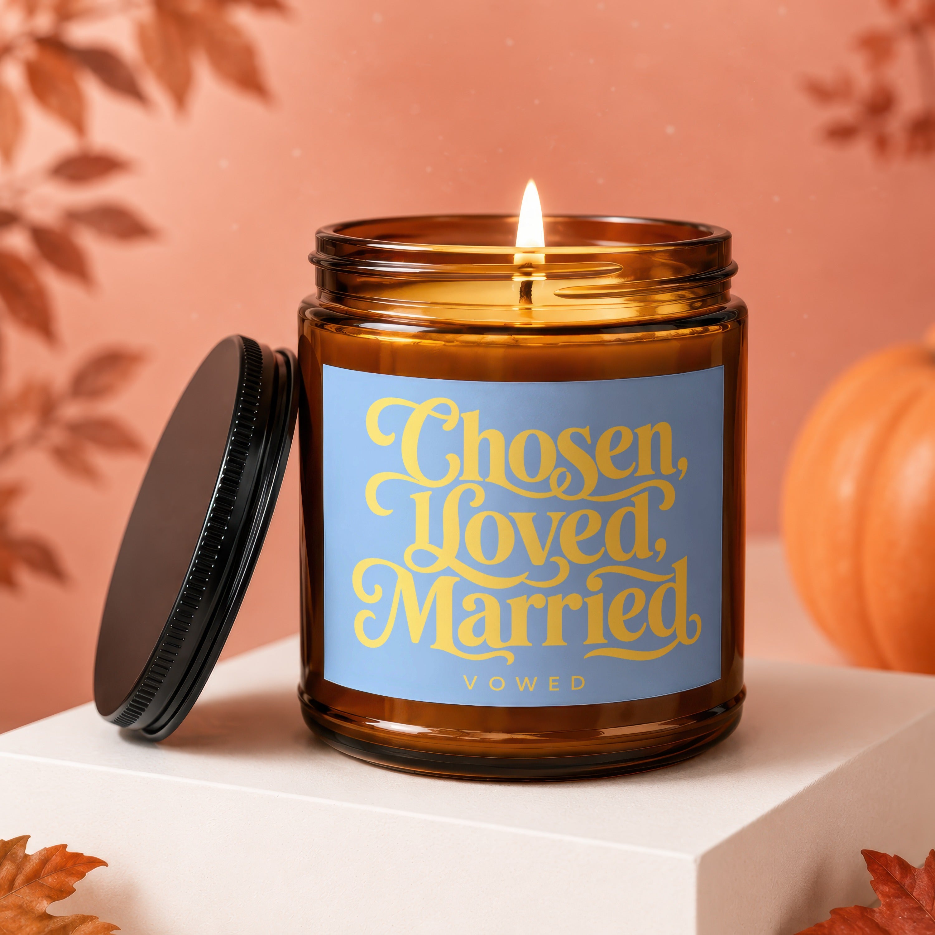 Amber glass candle with lit flame, lid off, and text "Chosen, Loved, Married VOWED".