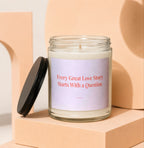 Glass candle with black lid and pink label reading "Every Great Love Story Starts With a Question."