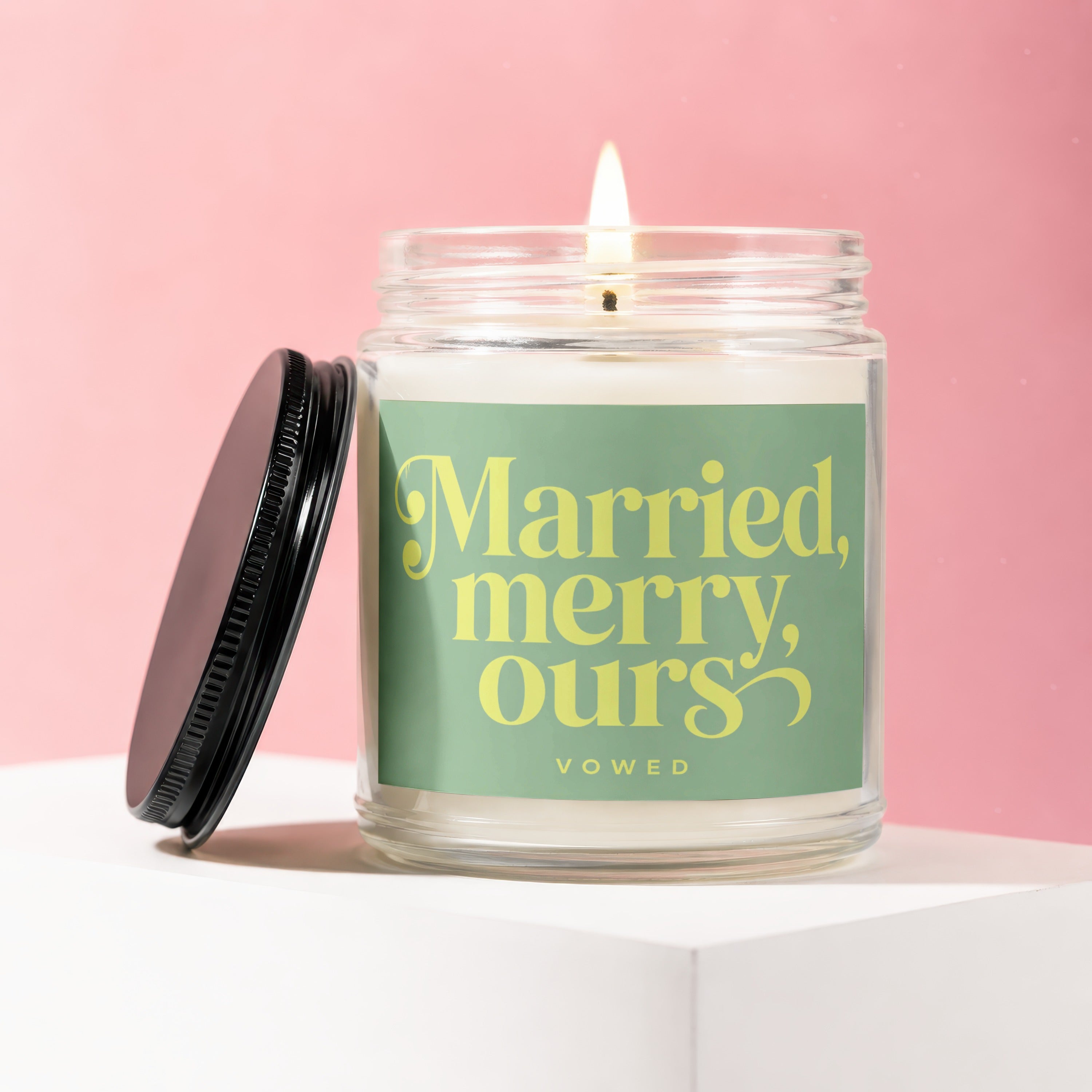Glass candle with lit wick and black lid. Label reads "Married, merry, ours VOWED".