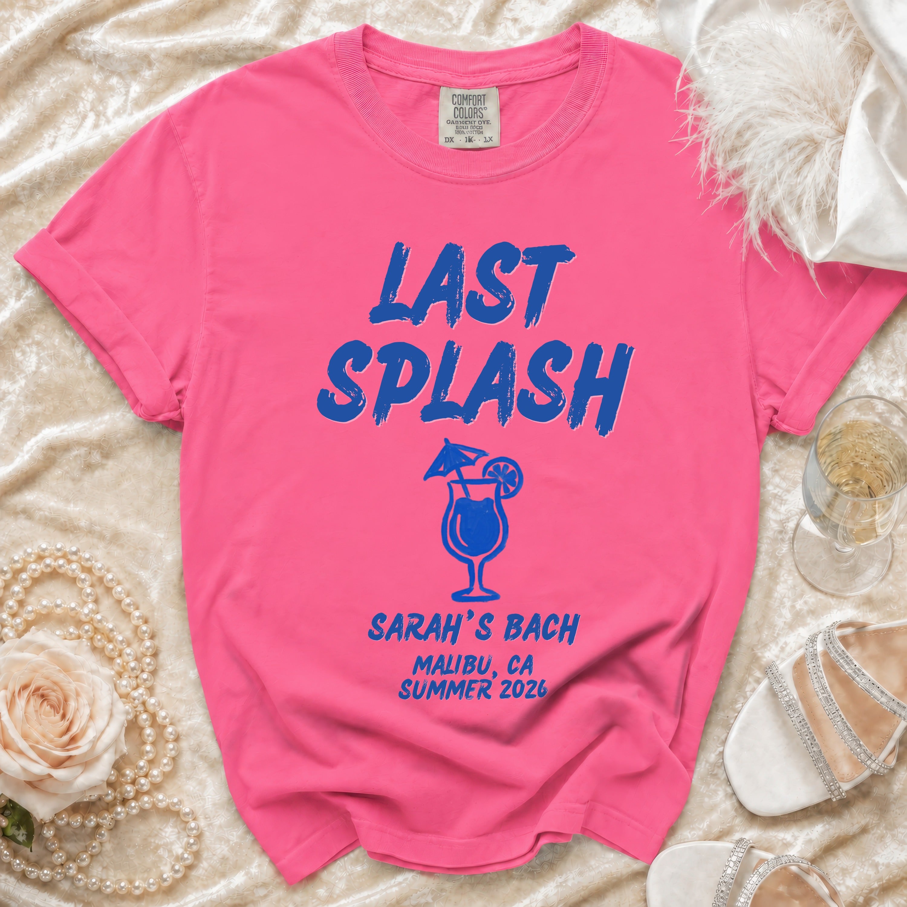Pink t-shirt with "LAST SPLASH" in blue text, cocktail graphic, and "SARAH'S BACH MALIBU, CA SUMMER 2026".