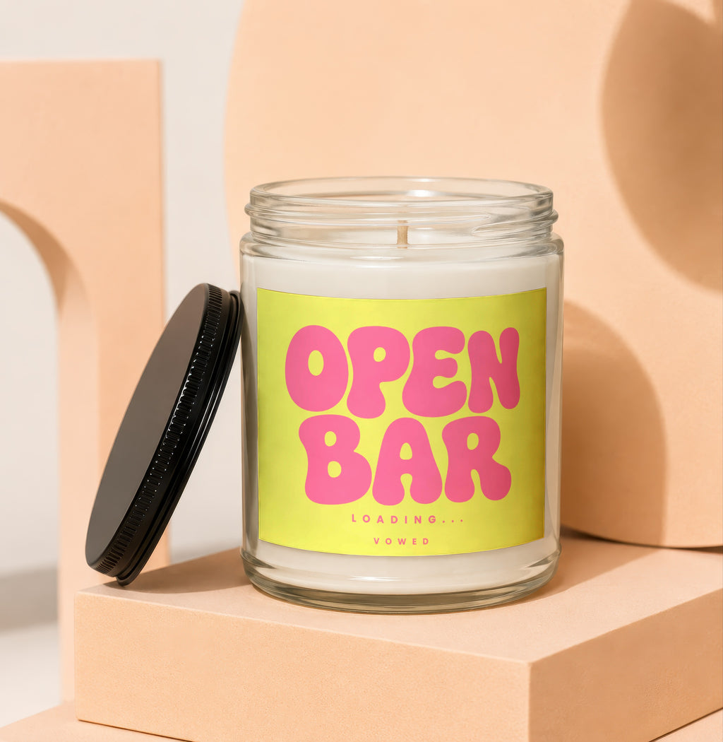 Glass jar candle with yellow label reading "OPEN BAR LOADING... VOWED".