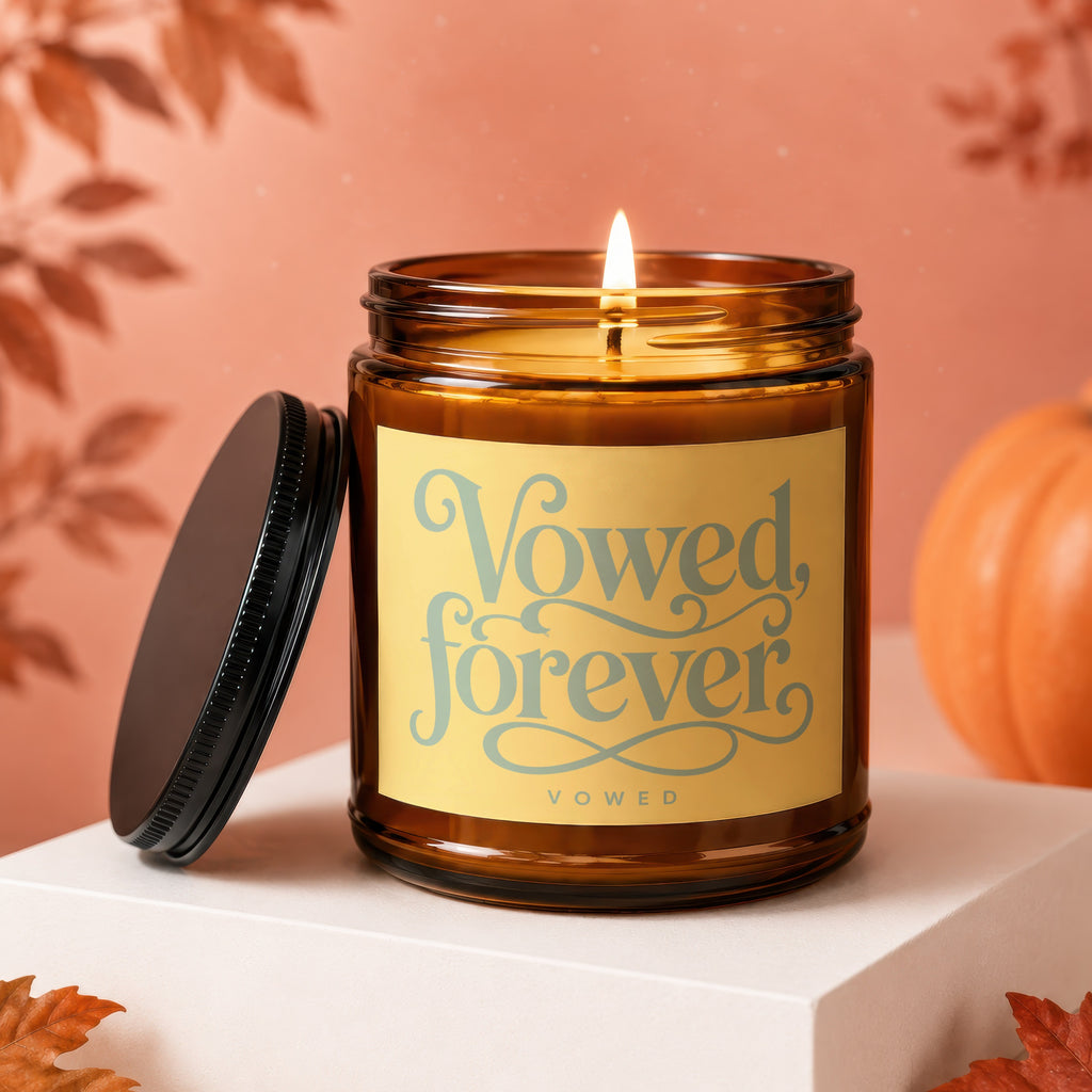 Amber jar candle with lit wick, "Vowed, forever" text, and black lid.